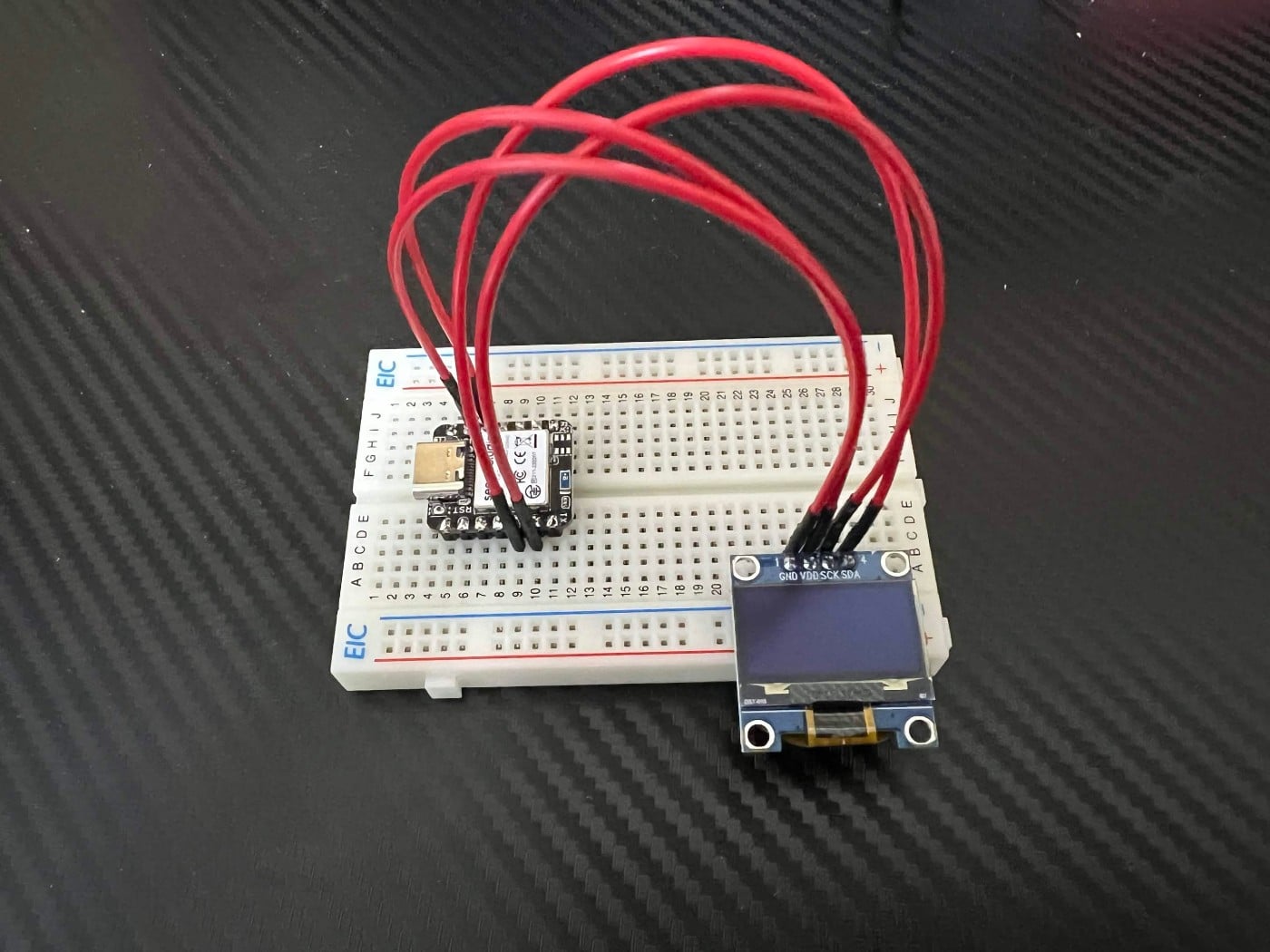 ブレッドボード上で赤いジャンパ線でつないだXIAOとOLED